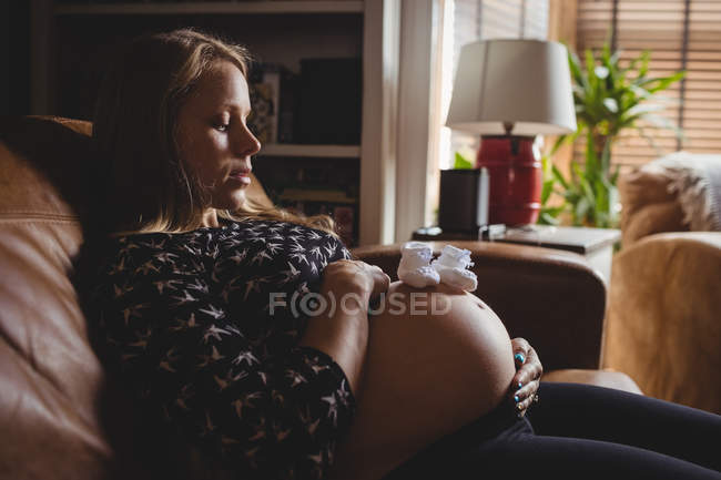 Пара детских носков на животе беременной женщины дома — стоковое фото