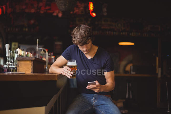 Homem usando telefone celular enquanto toma um copo de cerveja no bar — Fotografia de Stock