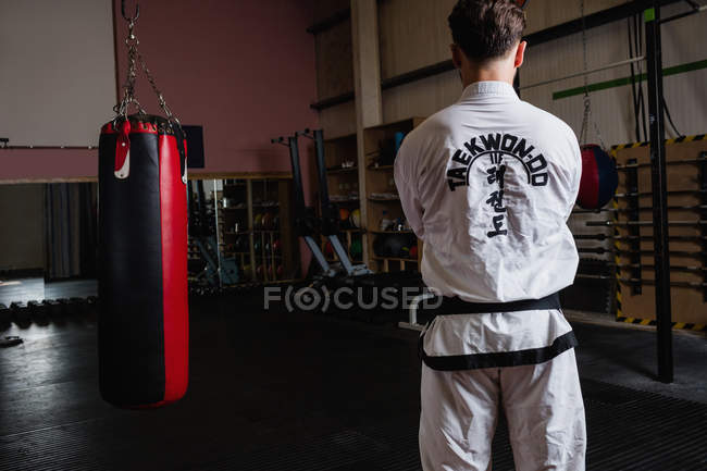 Вид сзади на человека, стоящего рядом с боксерской грушей в фитнес-студии — стоковое фото