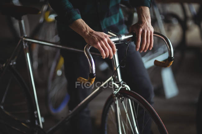 Mid-section of mechanic standing with bicycle in bicycle shop — Stock Photo