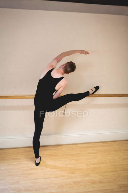 Vista trasera de Ballerino estirándose en barra mientras practica danza de ballet en estudio - foto de stock