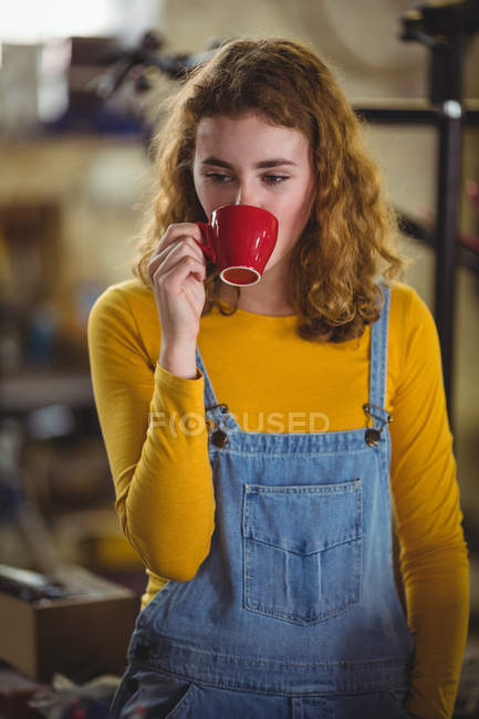 Задумчивая женщина, выпившая чашку кофе в магазине велосипедов — стоковое фото