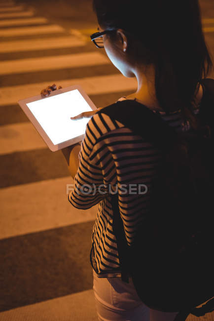Visão traseira da jovem mulher usando tablet digital na rua à noite — Fotografia de Stock
