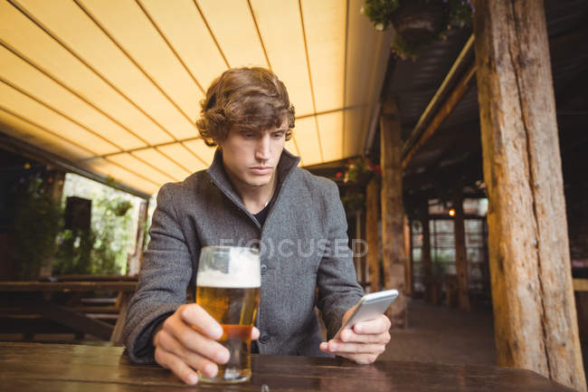 Hombre usando el teléfono móvil mientras toma un vaso de cerveza en el bar - foto de stock