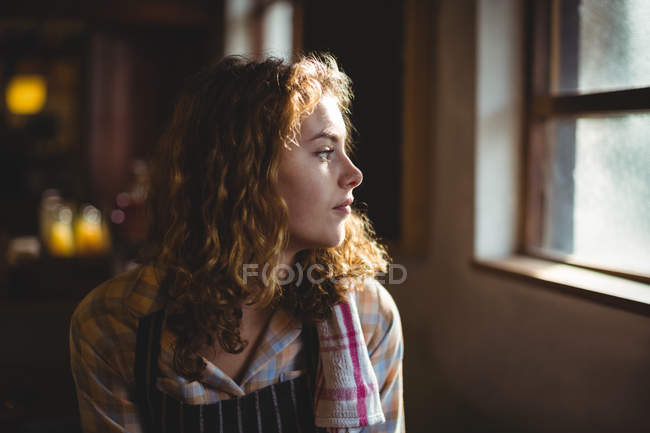 Nachdenkliche Kellnerin blickt durch Fenster in Werkstatt — Stockfoto