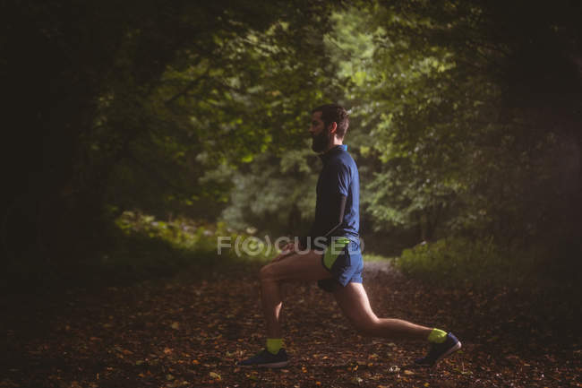 Спортсмен, що виконує вправи з розтягування в лісі — стокове фото