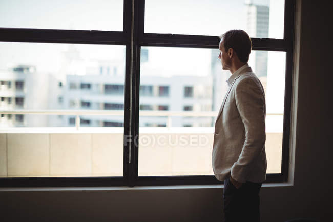 Uomo d'affari premuroso che guarda attraverso la finestra in ufficio — Foto stock