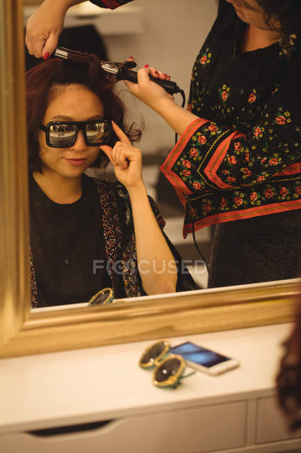 Femme élégante en lunettes de soleil se faire coiffer dans un salon de coiffure professionnel — Photo de stock
