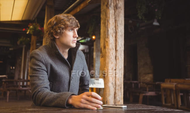Uomo premuroso seduto al bar con un bicchiere di birra sul tavolo — Foto stock