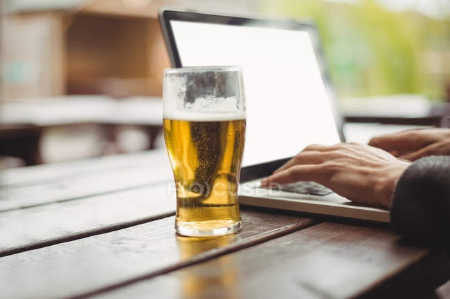 Чоловік використовує ноутбук зі склянкою пива на столі в барі — стокове фото
