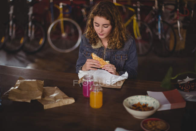 Mulher sentada à mesa e comendo sanduíche na loja de bicicletas — Fotografia de Stock