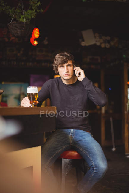 Чоловік говорить на мобільному телефоні в барі зі склянкою пива в руці — стокове фото