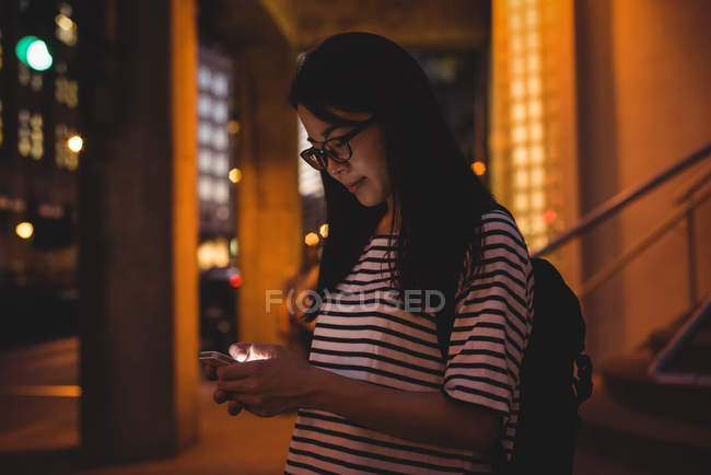 Mujer joven usando el teléfono móvil en el pasaje por la noche - foto de stock