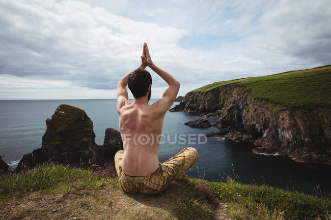 Rear view of man performing yoga on cliff — Stock Photo