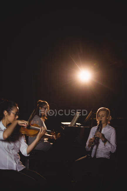 Три студентки играют на пианино, кларнете и скрипке в студии — стоковое фото