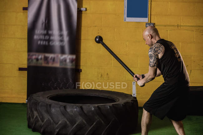 Вид сбоку тайского боксера, бьющего по шинам кувалдой в фитнес-студии — стоковое фото