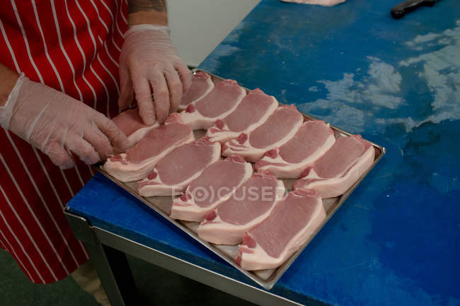 Manos de carnicero organizando filetes en bandeja en la carnicería - foto de stock