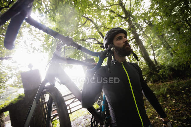Atleta llevando una bicicleta en el bosque - foto de stock
