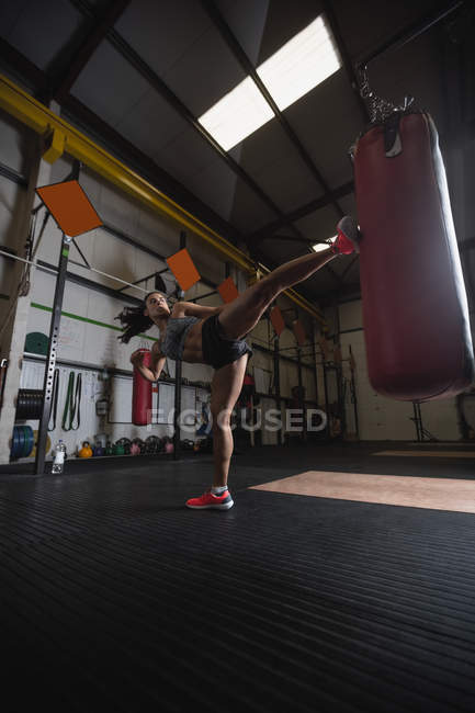 Vista a basso angolo del pugile femminile che pratica boxe con sacco da boxe in palestra — Foto stock