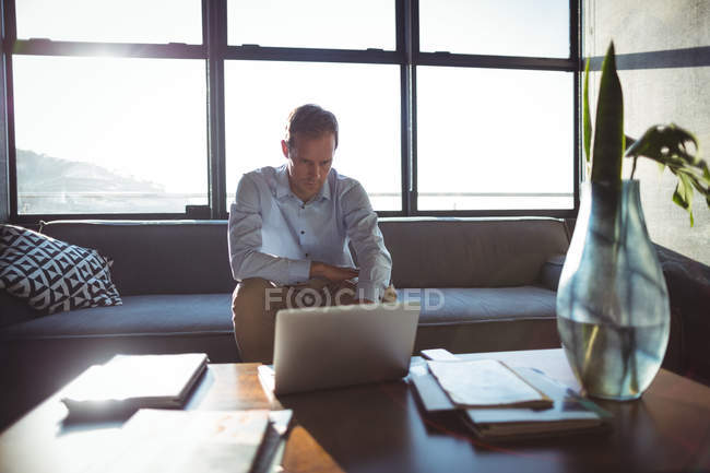 Homme d'affaires utilisant un ordinateur portable dans le bureau contre la lumière du soleil — Photo de stock