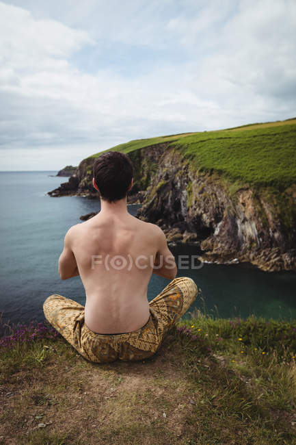 Вид ззаду людини, що виконує йогу на скелі — стокове фото