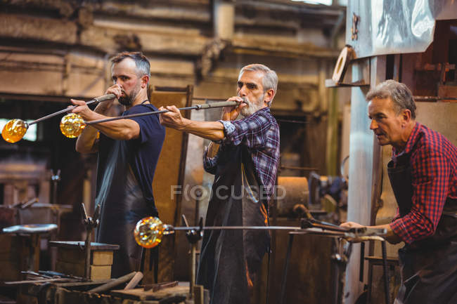 Team of glassblowers shaping a glass on the blowpipes at glassblowing factory — Stock Photo