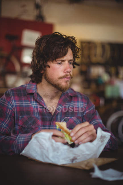 Man sitting at table and eating sandwich in bicycle shop — Stock Photo