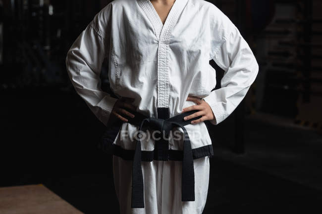 Sección media de la mujer de karate de pie con las manos en las caderas en el gimnasio - foto de stock