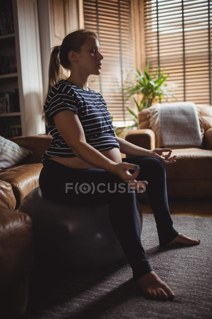 Femme enceinte effectuant du yoga sur balle de fitness dans le salon à la maison — Photo de stock