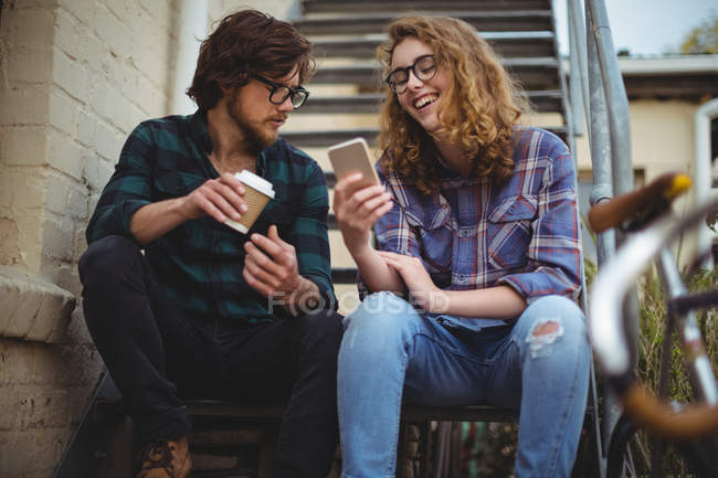 Couple assis sur les escaliers et utilisant un téléphone portable à l'extérieur de la maison — Photo de stock