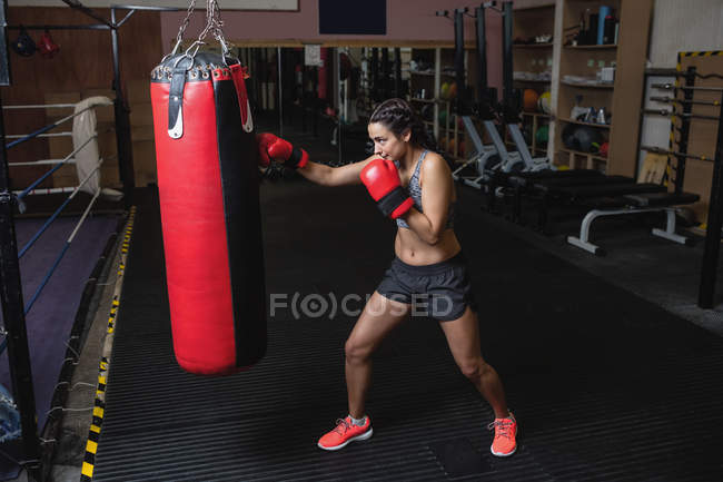 Vista laterale del pugile femminile che pratica boxe con sacco da boxe in palestra — Foto stock
