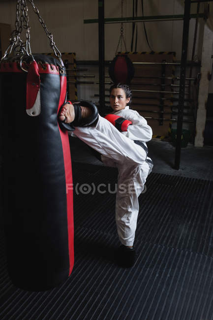 Sportswoman practicing karate with punching bag in fitness studio — Stock Photo