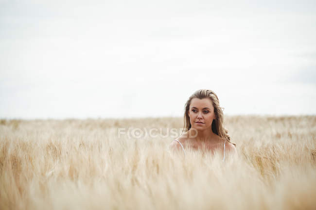 Femme debout dans le champ de blé par une journée ensoleillée dans la campagne — Photo de stock