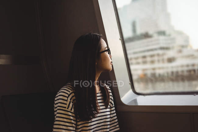 Jeune femme réfléchie regardant par la fenêtre tout en voyageant dans le navire — Photo de stock