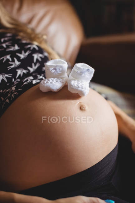 Imagem cortada de Par de meias de bebê na barriga da mulher grávida em casa — Fotografia de Stock