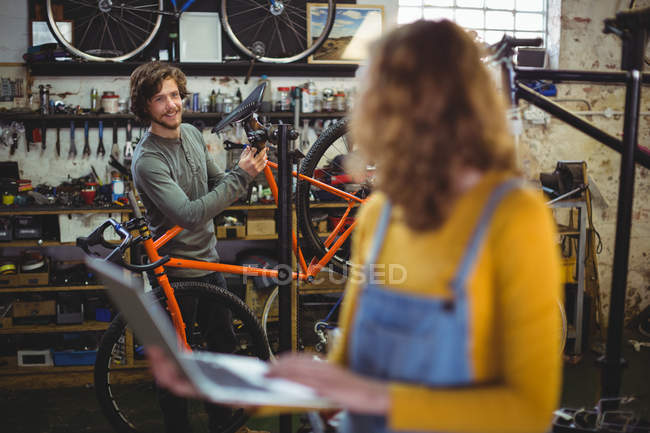 Mecânica interagindo ao usar laptop na loja de bicicletas — Fotografia de Stock