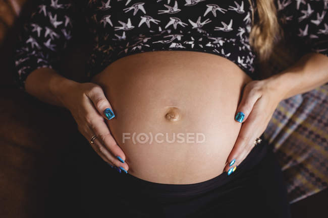Immagine ritagliata di donna incinta rilassante e commovente pancia in soggiorno — Foto stock