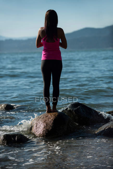 Rear view of woman practicing yoga on rock at ocean beach — Stock Photo