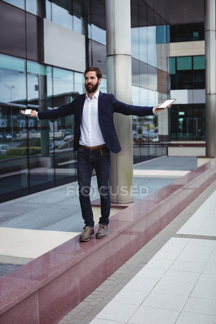 Uomo d'affari che tiene il telefono cellulare e tablet digitale mentre cammina sul passaggio — Foto stock