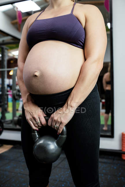 Imagen recortada de mujer embarazada levantando la campana de la tetera en el gimnasio - foto de stock