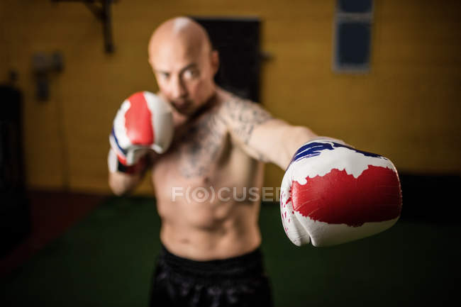 Selective focus of shirtless muscular Thai boxer practicing boxing in gym — Stock Photo