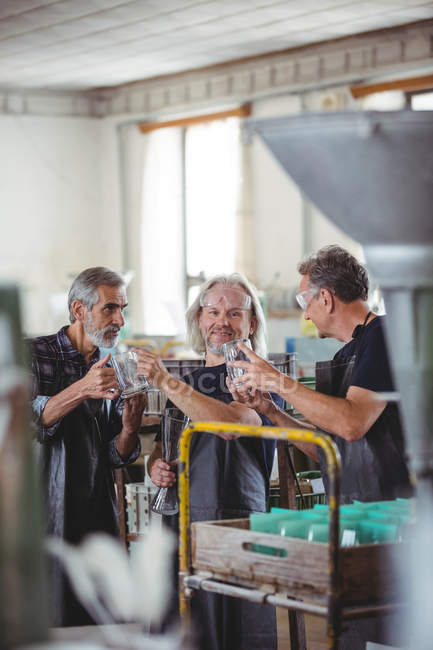 Souffleurs de verre interagissant tout en examinant vase en verre dans l'usine de soufflage de verre — Photo de stock
