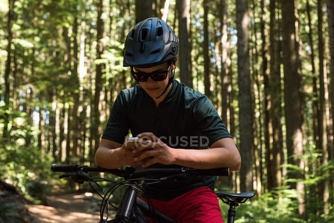 Чоловічий велосипедист використовує мобільний телефон у лісі на сонячному світлі — стокове фото