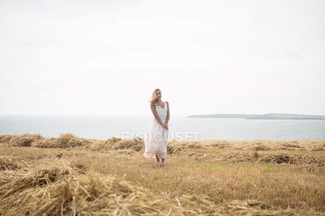 Beautiful blonde woman standing in field near river — Stock Photo
