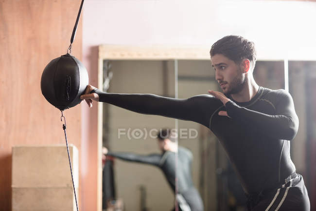 Vue latérale du boxeur masculin pratiquant la boxe avec sac de boxe dans un studio de fitness — Photo de stock