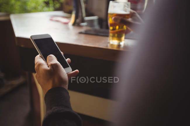 Homem usando telefone celular com copo de cerveja na mão no bar — Fotografia de Stock