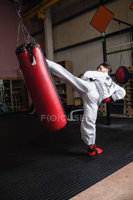 Visão traseira do homem praticando karatê com saco de perfuração no estúdio de fitness — Fotografia de Stock