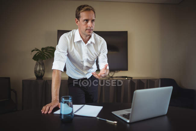Бізнесмен спирається на офісний стіл і жестикулює, пояснюючи при цьому — стокове фото