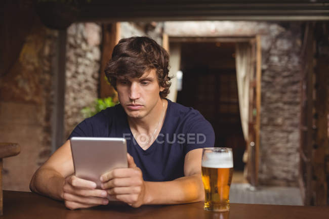 Человек с цифровой планшет со стеклом пива на столе в баре — стоковое фото