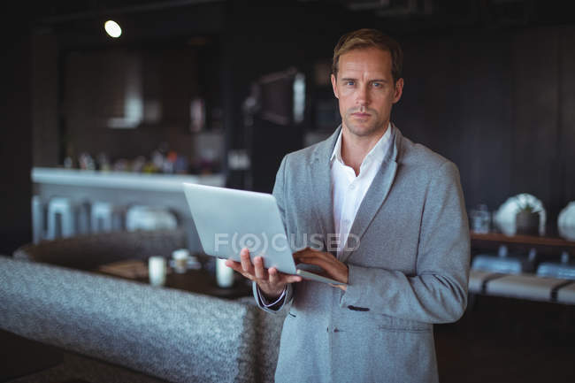 Portrait of a businessman standing with a laptop in cafe — Stock Photo